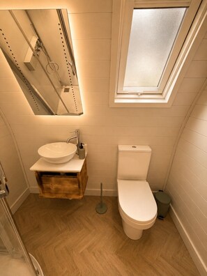 Ein kleines Badezimmer mit einem Holzkosmetikschrank, einem weißen Waschbecken, einer Toilette und einem Oberlicht.