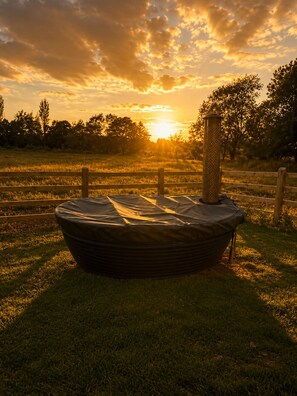 A hot tub in a grassy field with a sunset in the background.