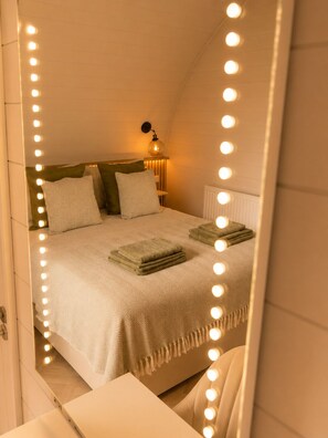 Ein Schlafzimmer mit Bett, Nachttischlampen und einem beleuchteten Spiegel.