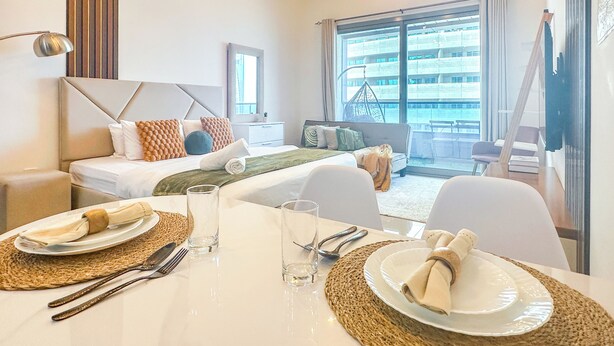Ein modernes Hotelzimmer mit Bett, Sitzecke, Esstisch und großen Fenstern mit Blick auf die Stadt.