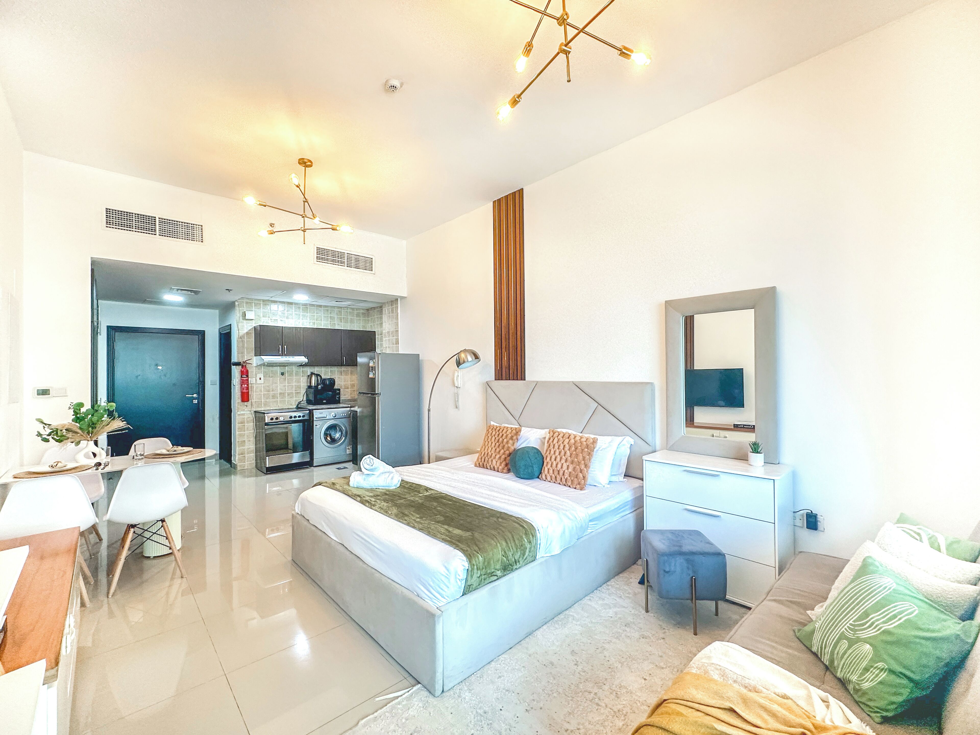 Habitación de hotel moderna con una cama grande, un escritorio, una silla, una mesita, un sofá, un espejo y una kitchenette.