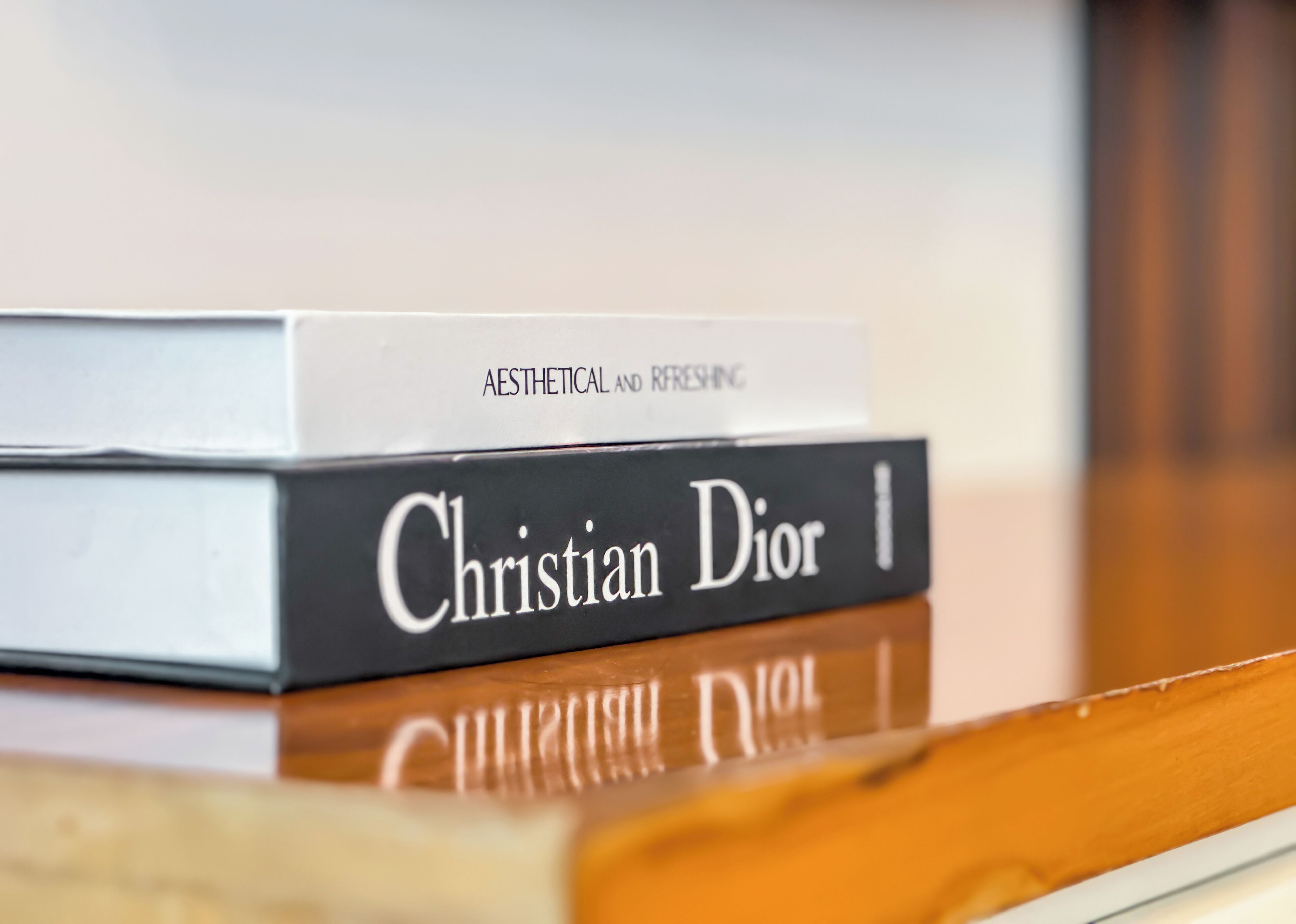 Twee boeken met de titels 'Aesthetic and Refreshing' en 'Christian Dior' op een houten oppervlak.