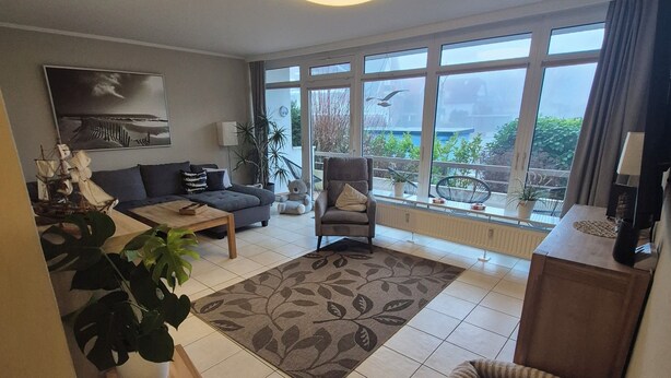 A spacious living room with a large window, a sofa, a chair, and a small table. - Großraumbude 44 - House Baltic (Grömitz)