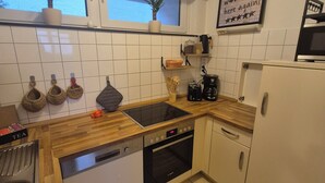 A modern kitchen with a dishwasher, oven, and a coffee maker. There are two potted plants on the windowsill and a 'Guest Check' sign on the wall. - Großraumbude 44 - House Baltic (Grömitz)