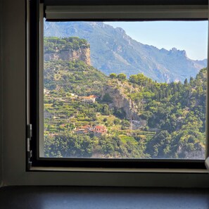 Blick aus dem Fenster auf eine gebirgige Landschaft mit terrassenförmig angelegten Häusern und einer markanten Felswand.
