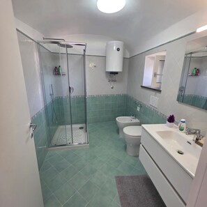 Een badkamer met een glazen douchecabine, toilet, bidet en een wastafel met spiegel.