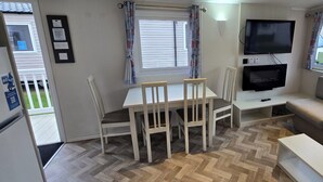 Un espace de vie compact comprenant une table à manger, deux chaises, un téléviseur et un petit coin salon.