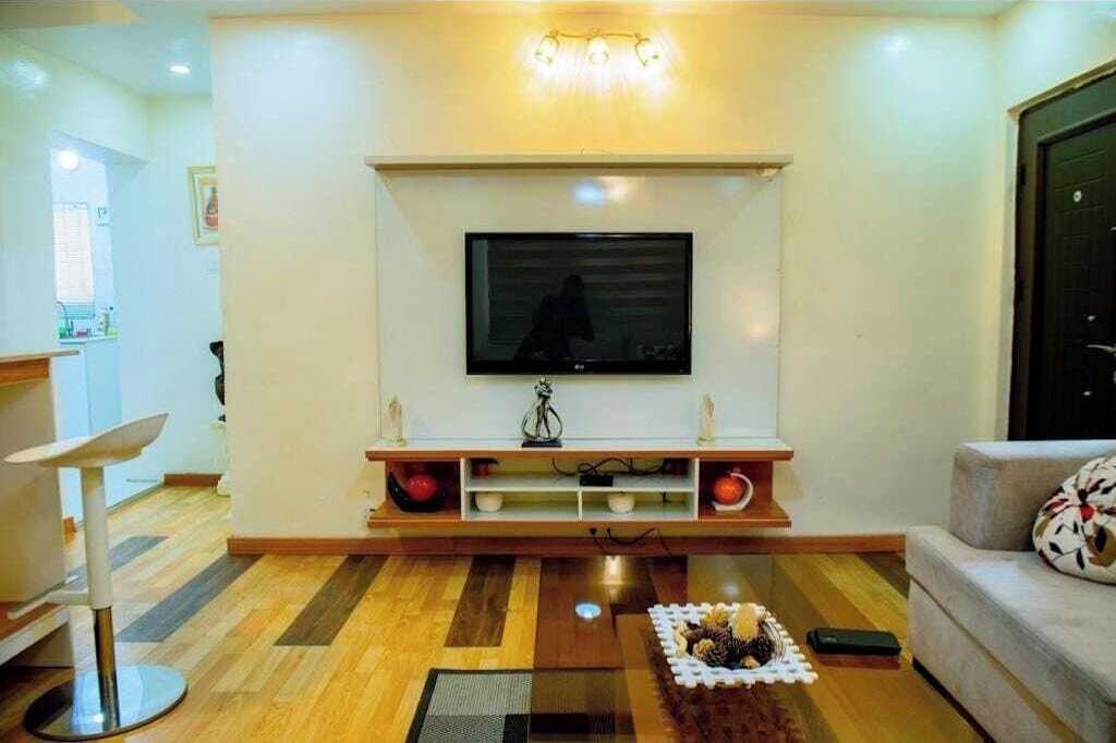 Una sala de estar con una televisión de pantalla plana montada sobre un soporte de madera, una mesa de centro con objetos decorativos y un sofá con un cojín estampado.