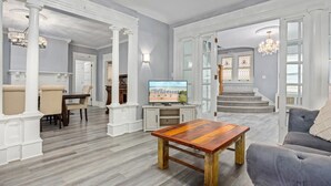 Un salon spacieux avec une table basse en bois, un canapé gris et un téléviseur posé sur un meuble blanc.