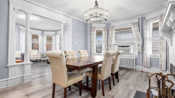 Une salle à manger spacieuse, avec une table en bois et six chaises rembourrées, un lustre et une vue sur un escalier.