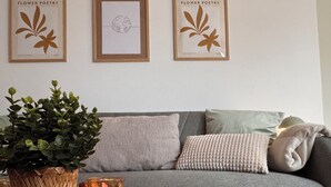 Un salon avec un canapé gris, un pot de fleurs en fibres tressées et deux bougies allumées posées sur un sous-verre en bois.