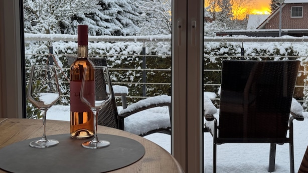Une table avec une bouteille et deux verres, une chaise, et une vue sur un paysage enneigé au coucher du soleil.