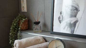 Un bagno ben organizzato con un mobile bagno in legno, un quadro incorniciato, una pianta in vaso e una piccola sveglia.