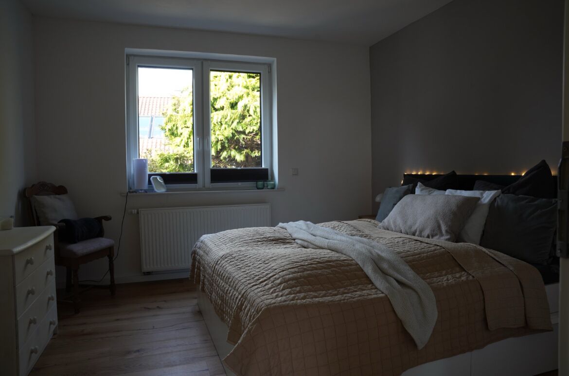 Une chambre à coucher avec un lit, une fenêtre, un radiateur, une chaise et une commode.