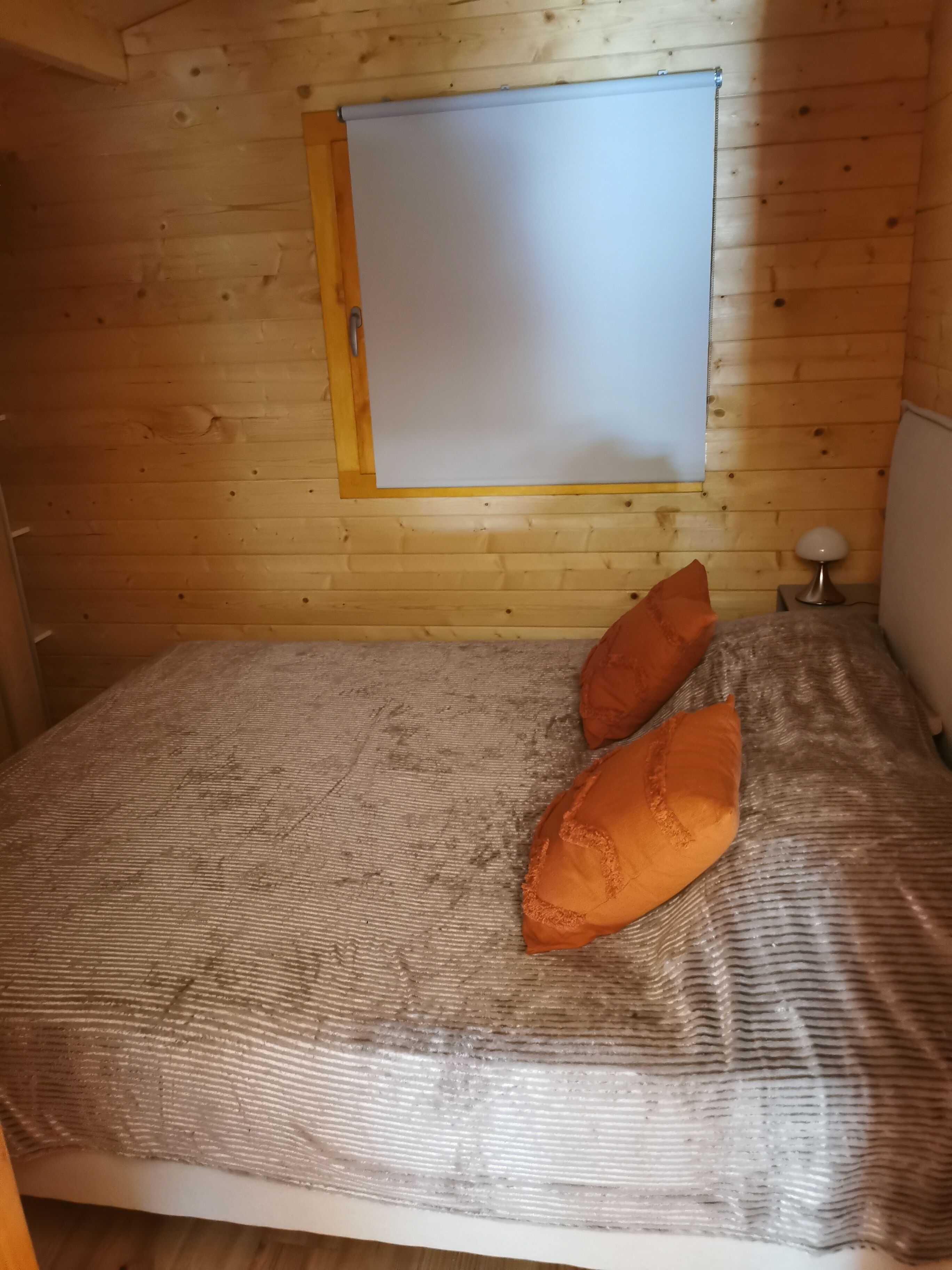 A wooden cabin room with a bed, two pillows, a nightstand, and a lamp.