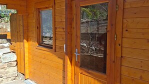 A wooden cabin with a stone foundation, wooden doors with glass panels, and a small window. - CHALET MARYVONNE LES VANS 07140 (Les Vans)