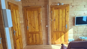 A wooden cabin interior with two wooden doors, a television mounted on the wall, and a purple chair. - CHALET MARYVONNE LES VANS 07140 (Les Vans)
