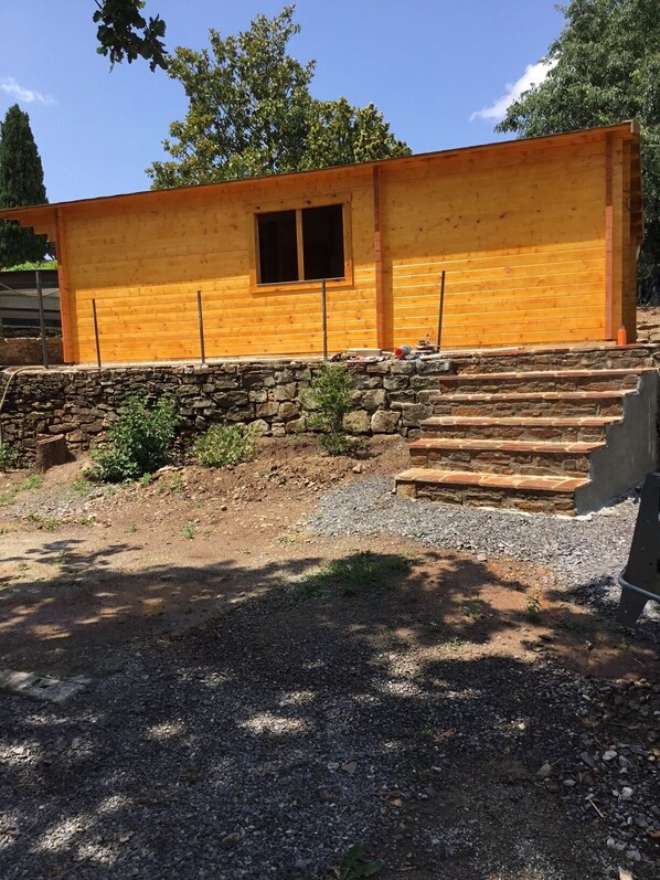 Eine Holzhütte mit Steinunterbau, einem kleinen Fenster und einer Steintreppe, die zu einer Tür führt.