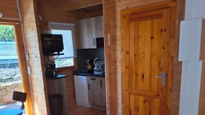 A cozy cabin interior with a wooden floor, a pink sofa, a television, a kitchen area, and a wooden door. - CHALET MARYVONNE LES VANS 07140 (Les Vans)