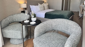 Ett modernt hotellrum med en säng, två fåtöljer, ett litet bord med en lampa och en krukväxt.