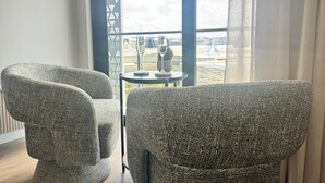 Ett rum med två grå stoppade fåtöljer, ett litet runt bord med en glasskiva och utsikt över en flygplats genom stora fönster.