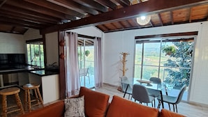 A modern living room with a large orange sofa, a dining table with chairs, and a kitchen area with stools. - Spacious house with 360° view of coffee plantations - Filandia (Filandia)