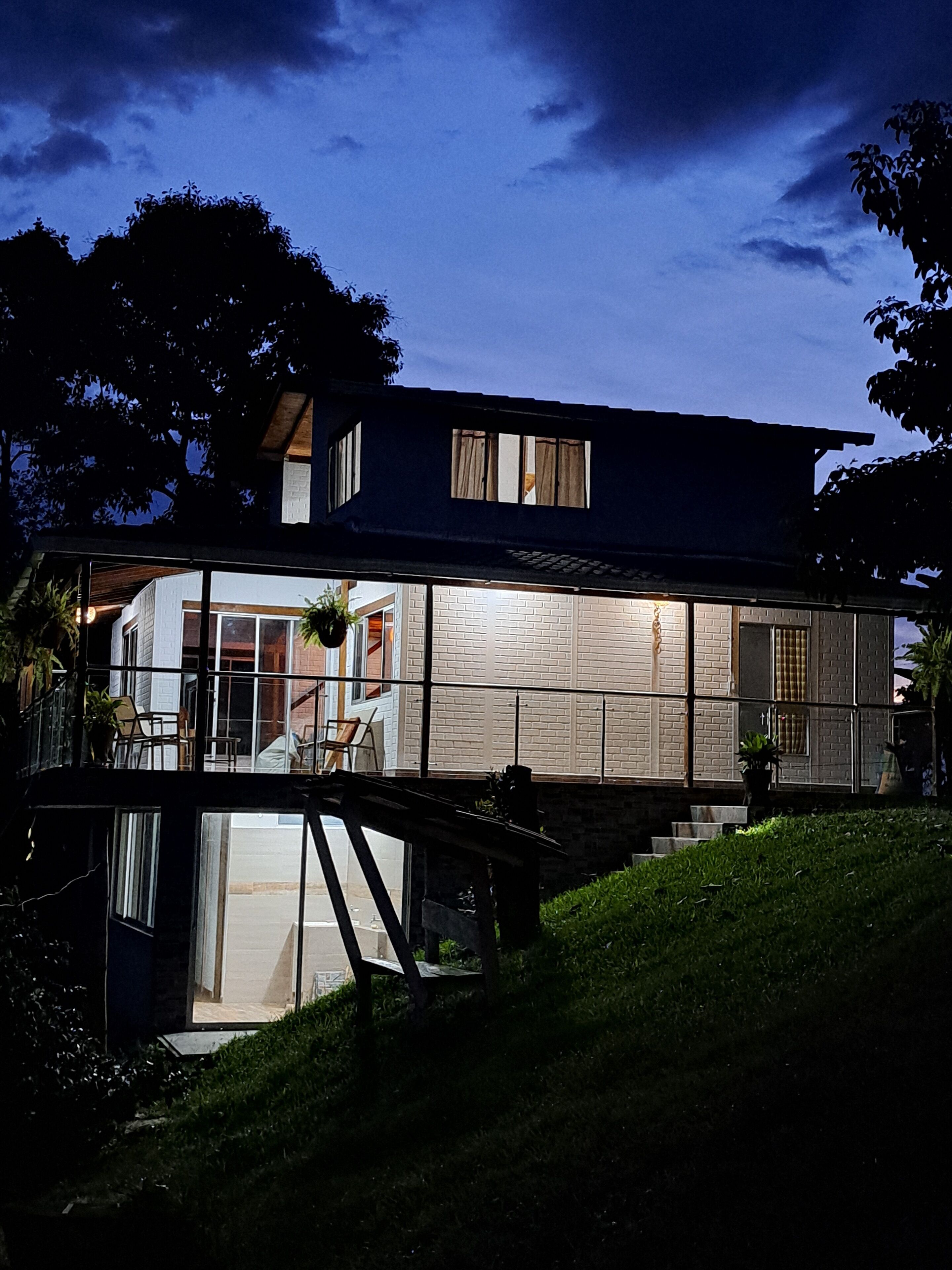 A modern house with a glass facade, a covered outdoor area, and a staircase leading to a deck.