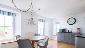 Eine moderne Küche mit einem runden Holztisch, grauen Stühlen und einer hängenden Leuchte.