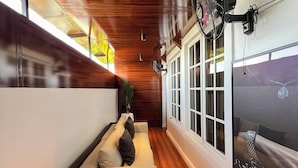 Et moderne interiør med træloft, en sort sofa med puder, en ventilator og et stort vindue med udsigt over bybilledet.