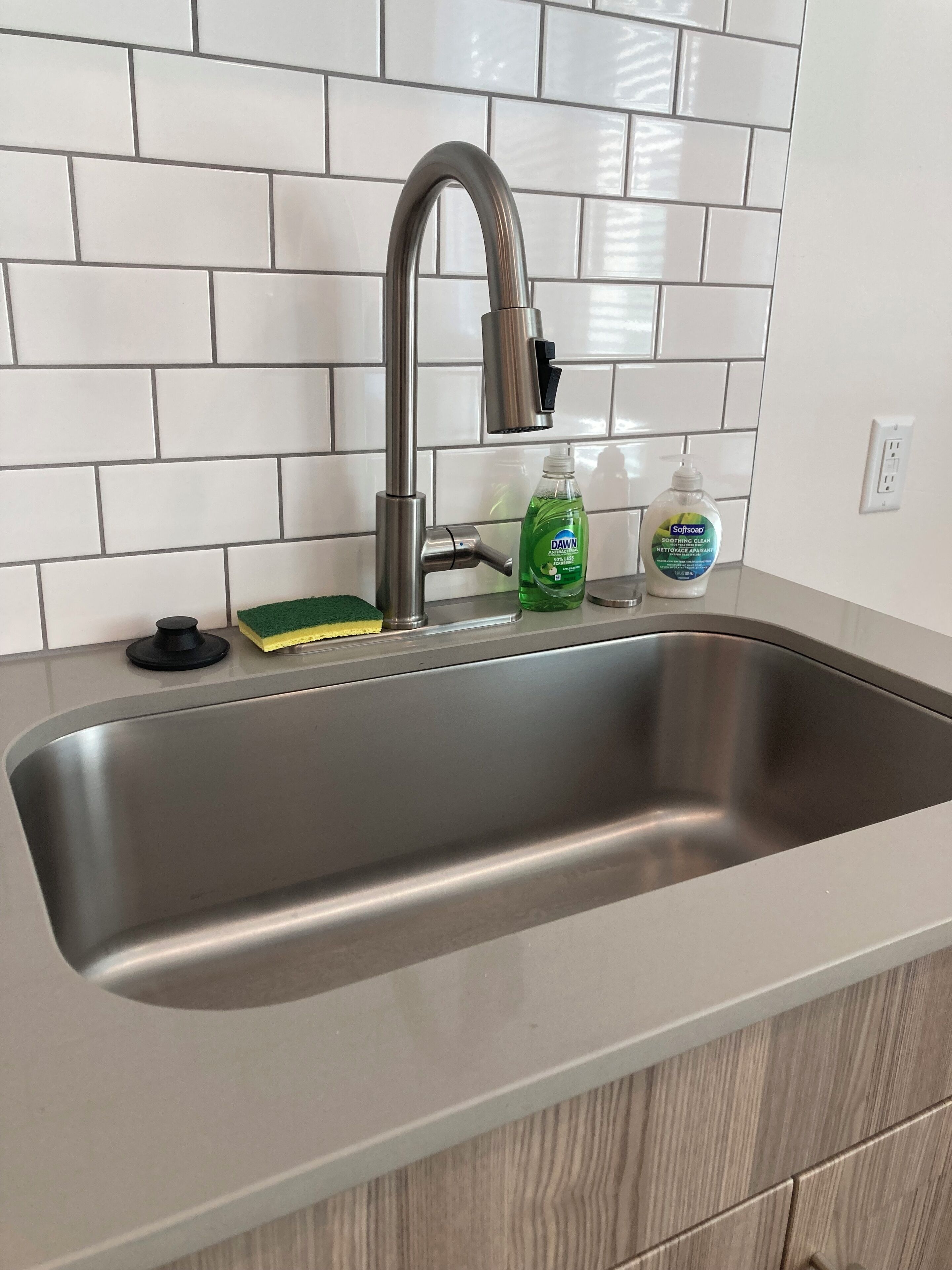 A stainless steel kitchen sink with a modern faucet, a soap dispenser, and a sponge.
