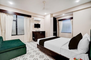 Une chambre d’hôtel avec un lit, un fauteuil vert, une télévision et un appareil de climatisation.