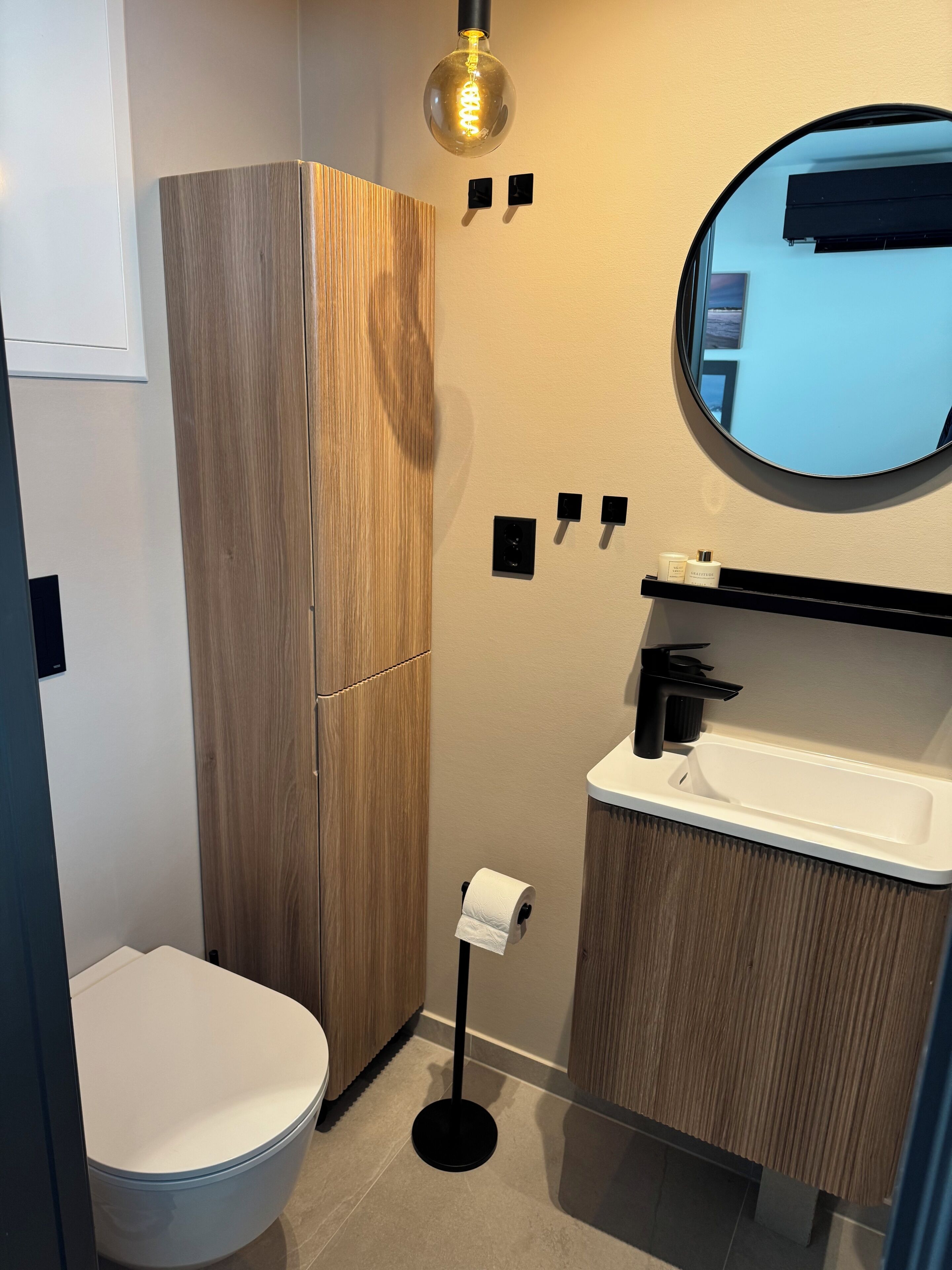 Et moderne badeværelse med toilet, træskab, vask og spejl.