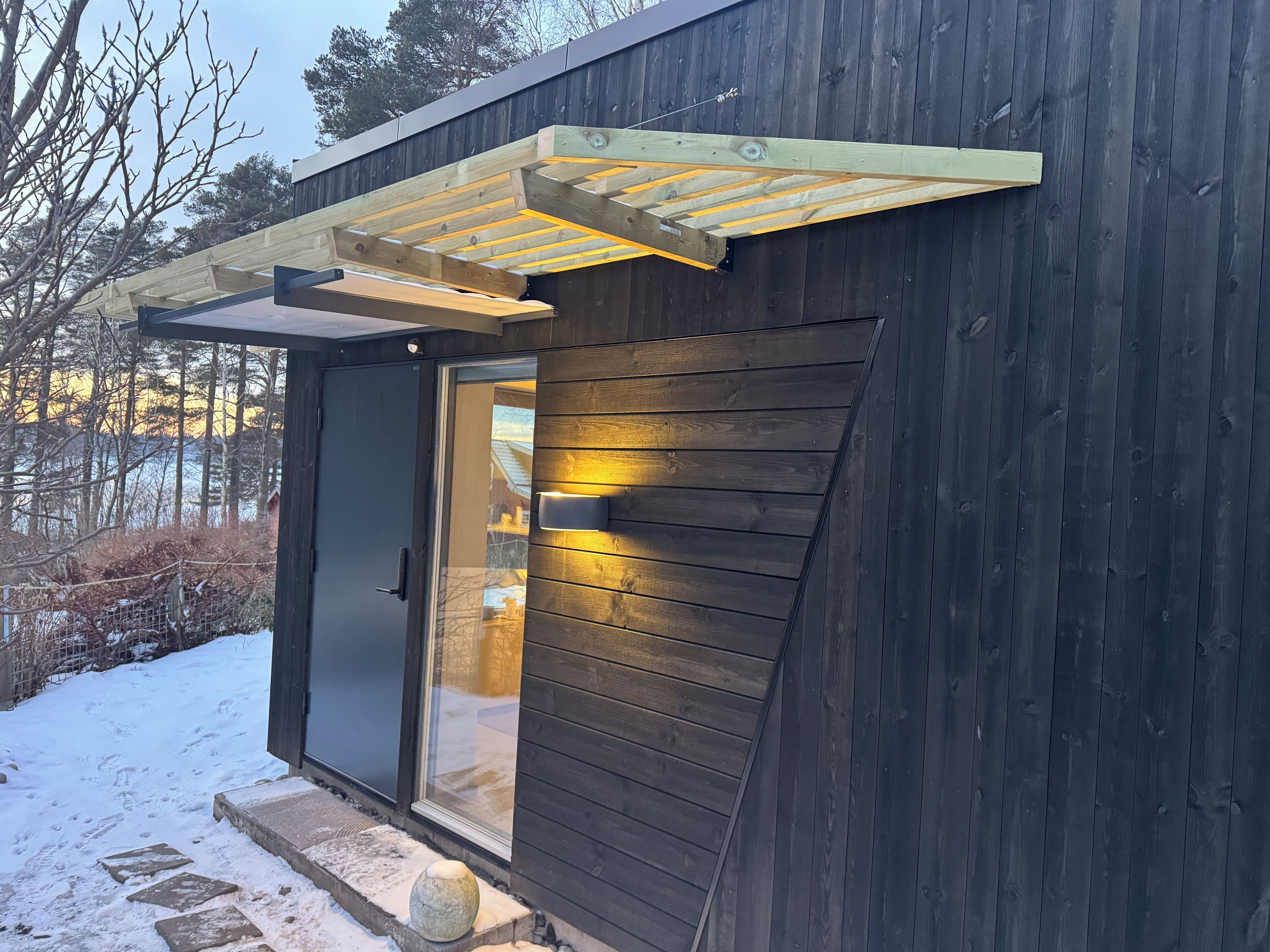 A wooden cabin with a glass door, a stone pathway, and a wooden pergola.