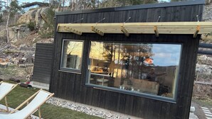 Un edificio moderno con grandes ventanales, una pérgola de madera y un patio con una silla y una mesa.