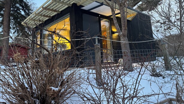 Una casa moderna con fachada de vidrio, rodeada de árboles y nieve.