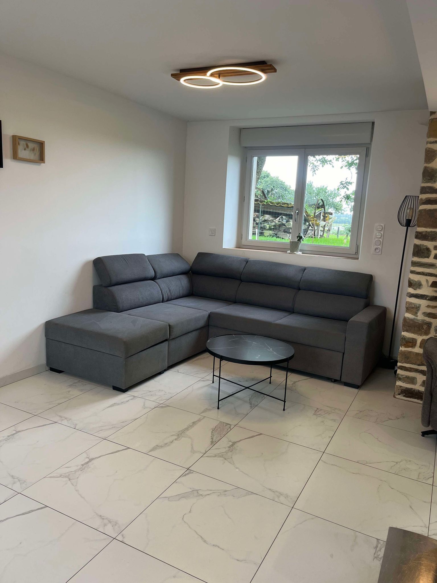A modern living room with a sectional sofa, a small round table, and a large window with a view of greenery.
