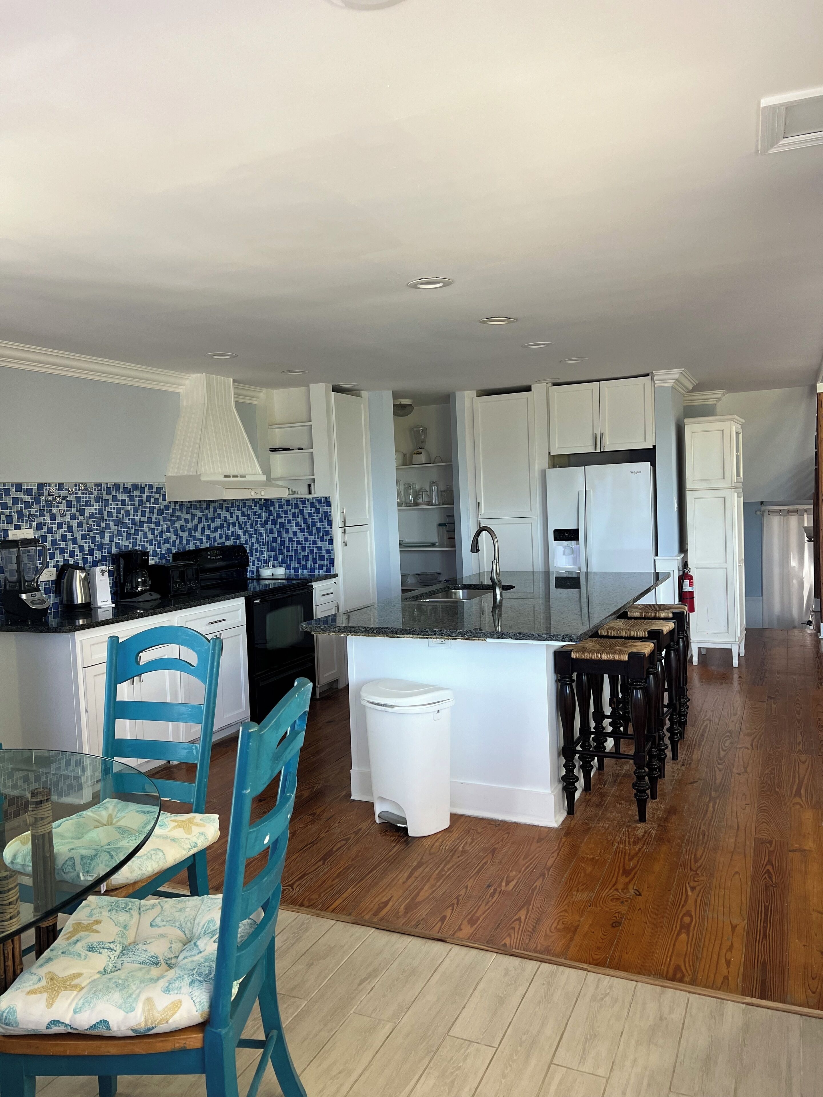Uma cozinha moderna com armários brancos, painel de azulejos azuis e uma ilha central com banquetas.