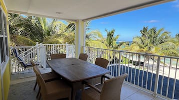 A covered outdoor area with a table and chairs, a view of the ocean, and a white railing.