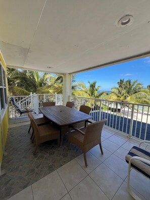 A covered outdoor area with a table and chairs, a view of the ocean, and a white railing.