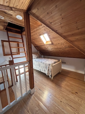 A loft bedroom with a wooden ceiling, a skylight, a bed, and a wooden ladder.