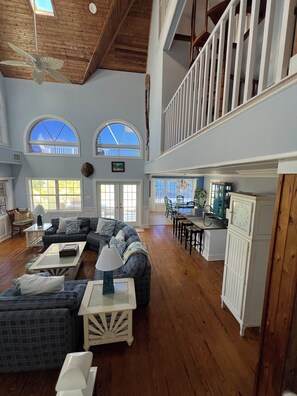 A spacious living area with a high ceiling, wooden beams, and a dining area with a view.