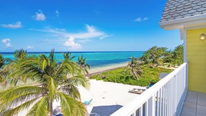 A beachfront property with a balcony overlooking the ocean, palm trees, and a white sandy beach.