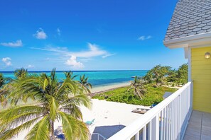A beachfront property with a balcony overlooking the ocean, palm trees, and a white sandy beach. - Beach House ~ Beachfront Retreat with Kayaks, Pool & Hot Tub (Grand Cayman)