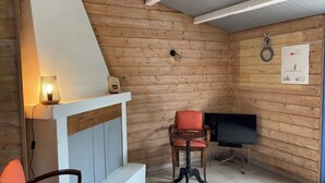 Una habitación acogedora con paredes de madera, un televisor, una silla roja y una mesita con una lámpara.