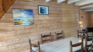 Pared de paneles de madera con dos cuadros enmarcados, una mesa de comedor con cuatro sillas y una mesita con una vela.