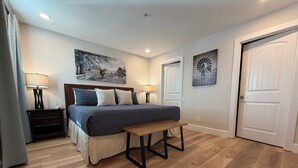 Ein Schlafzimmer mit einem Bett, Nachttischen, einer Bank, Holzböden und zwei Türen.