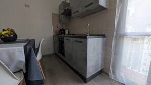 A compact kitchen with grey cabinets, a built-in oven, and a small dining area with a table and chairs. - La Mola B&B - a stone's throw from Viterbo and Rome (Vignanello)