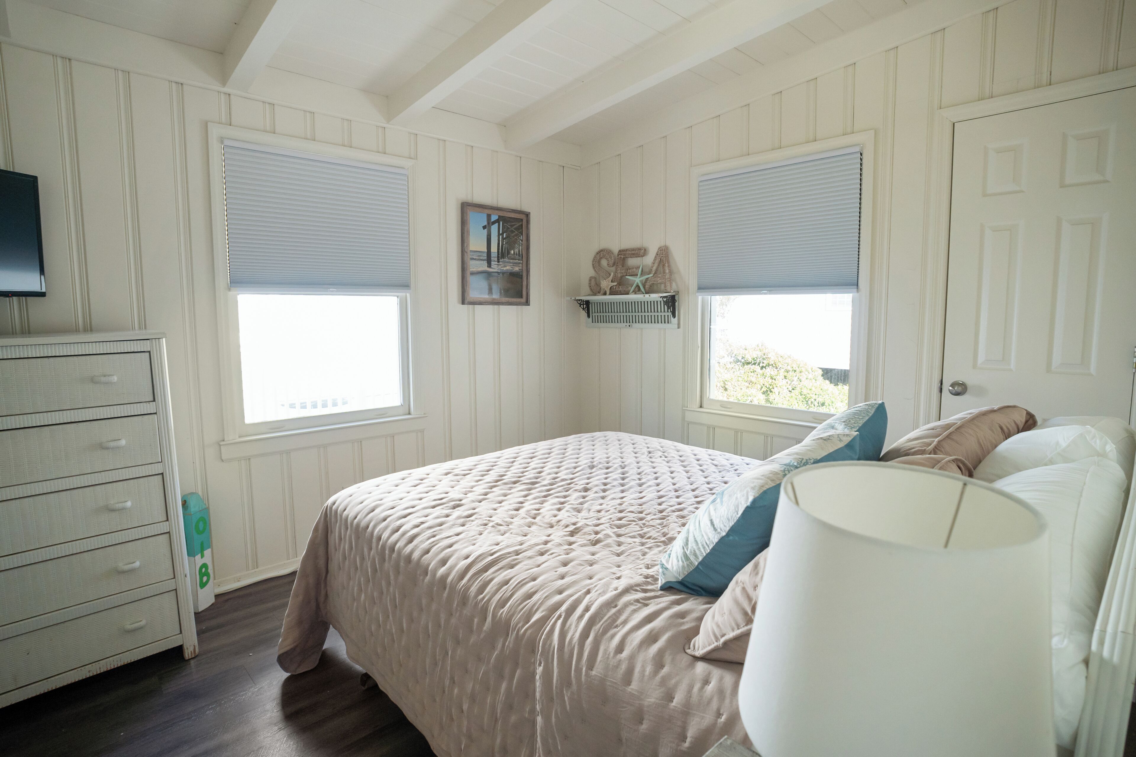 Une chambre à coucher comprenant un lit, une commode, des fenêtres et une étagère fixée au mur, ornée d’objets décoratifs.
