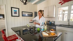 A kitchen with a central island, a sink, and a dining area with red chairs. - Sweet Tee: Costal Cottage, Steps from the Beach (Ocean Isle Beach)