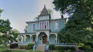 A large, two-story house with a prominent tower, a front porch with steps, and a flagpole. - Charming & Spacious Historic Charlotte Home- in the heart of the city (Charlotte)